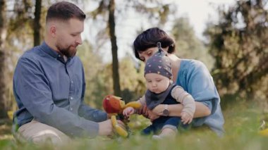 Bebekleriyle birlikte genç bir aile, yemyeşil bir parkta, doğa ve kaliteli zamanı kucaklayarak, rahatlatıcı bir pikniğin tadını çıkarıyor. Aile Yeşil Park 'ta Bebekle Huzurlu Piknik Yapıyor
