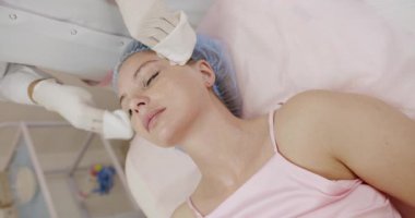 Klinik ortamda kadın bir hastaya nazik yüz bakımı sağlayan deneyimli bir sağlık uzmanı. Tedaviye ve sağlığa odaklan. Kozmetik Yüz Bakımı sırasında Profesyonel Tıbbi Bakım