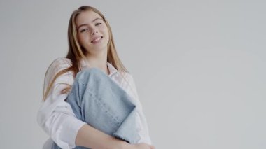 Uzun sarı saçlı, kameraya nazikçe gülümseyen beyaz bluz ve kot ceket giyen genç bir kadının portresi. Günlük kıyafetlerle poz verirken nazikçe gülümseyen genç kadın.