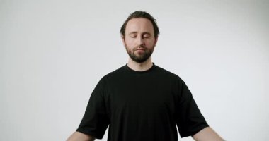 Sakallı bir adam beyaz stüdyo geçmişi üzerine meditasyon yapıyor. Siyah bir tişört giyiyor ve ellerini bir Mudra jestinde tutuyor. Barış ve farkındalık yayıyor. Farkındalık, rahatlama ya da sağIık..