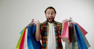 Heyecanlı adam renkli alışveriş torbaları taşıyor, harika anlaşmalara şaşırıyor. Perakende satış, tüketim ve alışveriş konuları için mükemmel. Sevinç ve memnuniyeti alışverişlerle ifade eder.