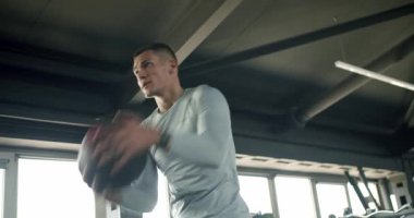 Genç, beyaz bir adam yoğun bir şekilde tıp topuyla modern bir spor salonunda eğitiliyordu. Odaklanma ve güç gösteriyordu. Modern Spor Salonu 'nda Tıp Balosu Odaklı Genç Adam Eğitimi