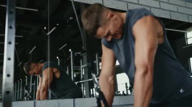 Kolsuz tişörtlü kararlı bir adam spor salonunda kablo kullanıyordu. Vücudunun üst kısımları ve formda kalmak için yoğun bir şekilde egzersiz yapıyordu. Modern Spor Salonunda Kablo Makinesinde Çalışan Genç Adam