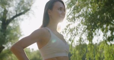 Spor kıyafetli genç bir kadının portresi çantasıyla dışarıda kameraya bakarak güneşli bir sabahta spor yapmak için parka geldi. Spor salonundaki kadın dışarıda egzersiz yapıyor. Kadın sporcu.