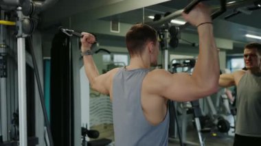 Spor salonunda çalışan, kablo makineleriyle sırt kaslarına odaklanan formda genç bir erkek. Yoğun fitness rutini. Genç Erkek Sporcu Modern Spor Salonunda Sırt Kaslarını Çalıştırıyor