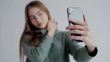 Yeşil kazaklı genç bir kadının kapalı bir ortamda akıllı telefonuyla selfie çekerken bulanık odak görüntüsü. Yeşil Süveterli Genç Kadın Akıllı Telefonla Selfie Çekiyor