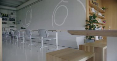 Bu çağdaş kafe zarif beyaz sandalyeleri, parlak ahşap masaları ve bitkilerle süslenmiş şık rafları olan minimalist tasarıma sahiptir. Yaşam tarzı ya da tasarım temaları için mükemmel..