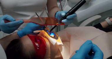 Hasta kadın, diş hekimine gidip stomatoloji kliniğindeki ultrason dişlerini muayene ediyor. Diş hekimi hastaların dişlerinde ultraviyole ışık kullanıyor. Diş hekimi hasta için diş temizliği yapıyor..