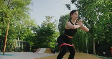 Genç bayan spor malzemeleriyle dışarıda egzersiz yapıyor. Aktif yaşam tarzı. Vücut geliştirme. Lastik bant bacak esnetme egzersizi yapmak için dört ayak kasları kasmak için..