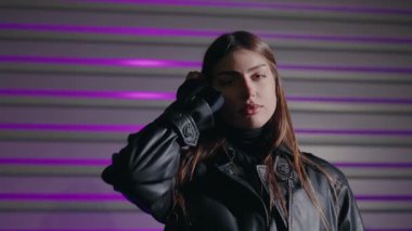 Uzun kahverengi saçlı genç kadın model renkli arka planda poz veriyor. Şık bir kız. Canlı neon renkli ışıklarla aydınlatılmış baştan çıkarıcı bir kadının portresi. Kameraya bakan güzel bir kızın portresi.