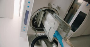 Kadın efendi sterilizasyon cihazından dezenfekte edilmiş tırnak aletlerini alıyor. Profesyonel kadın enfeksiyonların yayılmasını önlüyor ve müşteriler için hijyenik ortam sağlıyor. Müşteri güvenliği.