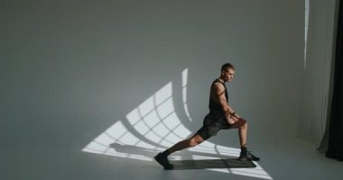 Atletik yapılı bir adam iyi aydınlatılmış bir stüdyoda fiziksel egzersizler yapar, dayanıklılık ve dayanıklılık gösterir. Atletik Genç Adam Stüdyo Ayarlarında Yoğun Çalışmalara Başladı