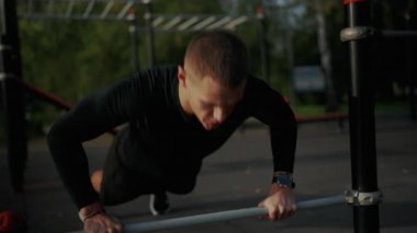Odaklanmış genç bir adam, park ortamında yatay bir bar kullanarak zorlu bir açık hava antrenmanına girişiyor. Barda Açık Hava Spor Programı Yapan Genç Adam