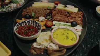Renkli sebzeler, lezzetli soslar ve çeşitli lezzetli ısırıklar içeren bir Akdeniz meze tabağının yüksek açılı görüntüsü. Mükemmel yemek fotoğrafçılığı sağlıklı ve canlı bir yemek sergiliyor..