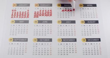 Mart 'ta kırmızı haçlı bir takvimde tarihi işaretleyen bir el resmi. Takvim, önemli tarih ve organizasyonların altı çizilerek, Ocak 'tan Aralık' a kadar ayları gösteriyor.