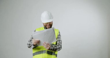 Heyecanlı inşaat mühendisi projesi hakkında harika haberler alıyor. Kasket ve güvenlik yeleği giyen adam proje başarısını kutluyor. Neşeli işçi beyaz arka plandaki belgeleri okur. Pozitif duygular