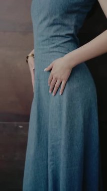 Elleri belinde dinlenen zarif mavi bir kot elbise giyen bir kadının yakın plan fotoğrafı. Görüntü stili, zarafeti ve modern modayı tasvir ediyor. Mavi Kum Elbiseli Zarif Kadın