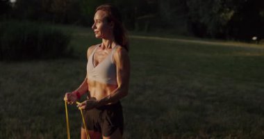 Spor kıyafetli güzel bir kadın direniş bandı egzersizleri yapıyor. Atletik kadın direniş bandıyla spor yapıyor. Kadın kaslarını şişiriyor. Kırmızı direniş bandıyla omuz egzersizi