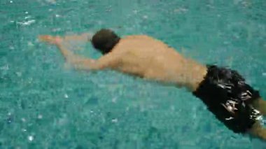 Erkek bir yüzücünün turkuaz bir yüzme havuzunda serbest stil felci uygulayarak çeviklik ve zindeliğin özünü yakaladığı dinamik bir çekim. Havuzda Antrenman sırasında Erkek Yüzücü Harekete Geçti