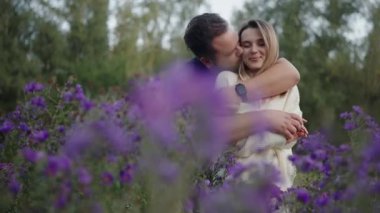 Genç bir çift, mor çiçeklerle çevrili yumuşak bir kucaklaşmayı paylaşır. Bu samimi an, romantizmin özünü ve doğal ortamdaki bağlantıyı yakalar..