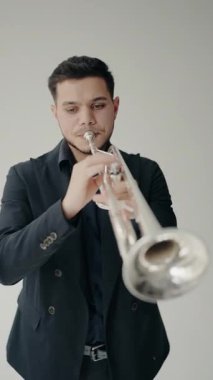 Takım elbiseli genç ve yakışıklı bir adam arzu ve ilhamla trompet çalar. Genç trompetçinin yakın eli. Dikey Video.