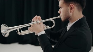 Takım elbiseli genç bir adam arzu ve ilhamla trompet çalar. Modern bir stüdyoda siyah arka planda trompet çalan bir erkek caz şarkıcısı. Genç trompetçinin eli.