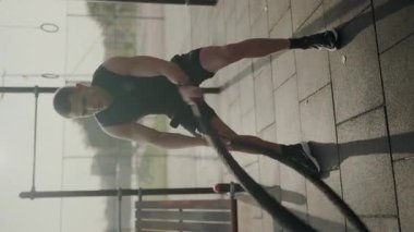 Odaklanmış erkek sporcu güneşli bir günde direnç bandı egzersizleri yaparak güç ve kararlılık gösteriyor. Genç sporcu, Yoğun Açık Hava Direniş Grubu Eğitimine girdi. Dikey video.
