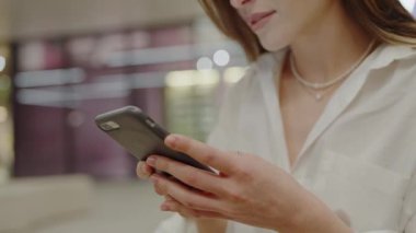 Modern, hafif ışıklandırılmış bir ortamda akıllı telefonuna odaklanan genç bir kadın, bir anlık bir bağlantı ya da dijital etkileşime işaret ediyor. Akıllı Telefonu Yumuşak Aydınlatma Ayarında Kullanan Genç Kadın