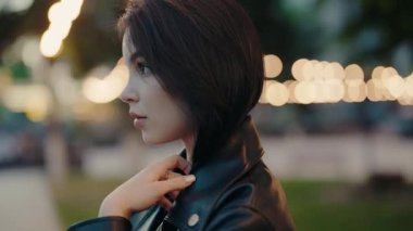 Siyah deri ceket giyen genç bir kadının yakın plan portresi. Gece karanlığında bulanık arka plan ışıklarıyla kameraya bakıyor. Bokeh Arkaplanlı Genç Kadın Portresi