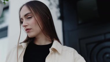 Uzun saçlı düşünceli bir kadın dışarıda dikiliyor, düşünceli ve günlük giysiler içinde. Arka planda bir mimari unsur var, bu da kentsel bir ortam olduğunu gösteriyor. Açık havada Kadın Pozu