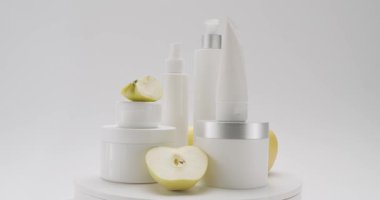 Kremalı parlak kozmetik kavanozu. Elma meyveli kavanozlar, şişeler ve tüpler beyaz arka planda güzellik tedavisi için dönerler. Farklı kozmetik şişeleri grubu.