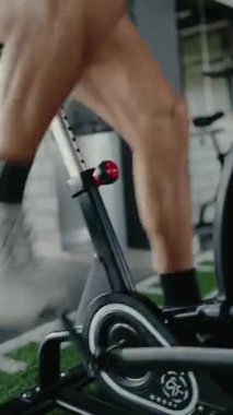 Genç bir adam spor salonunda kürek çekme makinesinde yoğun bir şekilde çalışıyor, kardiyo fitness ve dayanıklılığa odaklanıyor. İmaj kararlılığı ve atletik çabayı yakalıyor. Odaklanmış Adam Çalışıyor. Dikey 