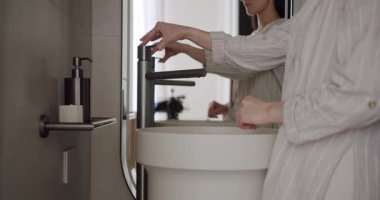 Modern bir banyoda minimalist tasarım unsurları olan şık bir havuzda ellerini yıkayan bir kadın. Modern Banyo 'da Minimalist Tasarımla El Yıkan Kadın