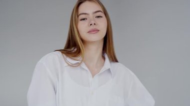 Beyaz gömlek giyen, kendine güvenen genç bir kadının portresi. Gri bir arkaplanda, sakin bir ifadeyle duruyor..