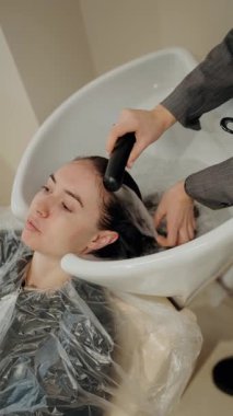 Kuaförde saçını yıkatan bir kadın. Profesyonel kuaför müşterisiyle ilgilenir. Güzellik salonu, saç bakımı, saç boyama. Sıcak atmosfer, rahatlama.