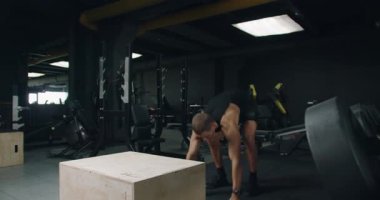 Karanlık temalı bir spor salonunda patlayıcı atlama yapan odaklanmış bir sporcu. Bu görüntü yoğun atletizm eğitimi ve adanmışlığı yakalar. Sporcu Sanatçısı Modern Spor Salonunda Zıpladı