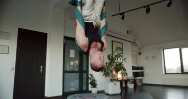Hafif stüdyodaki yoga seansı sırasında havadan hamakta baş aşağı asılı güçlü bir erkek resmi. Sınıfta çalışıyor, aero yogası yapıyor. Konsantrasyon. Spor etkinliği.