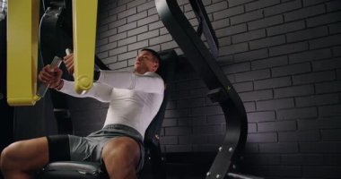 Spor salonunda göğüs pres makinesi kullanan kararlı bir adam. Forma kendini adamış ve yoğunluğunu gösteriyor. Spor salonundaki Göğüs Baskısı Makinesine Odaklanmış Adam Eğitimi