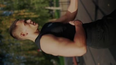 Yoğun bir bakışla dışarıda egzersiz yapan odaklanmış genç erkek sporcu, şehir zemininde kararlılık ve fiziksel güç sergiliyor. Genç Atletik Adam dışarıda gösteri yapıyor. Dikey video.