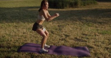 Atletik kadın spor yapıyor ve dışarıda fitness direnci bandıyla çömelme egzersizi yapıyor. Parkta kadın kalça kaslarını çalıştırıyor. Halk parkında direniş bandı eğitimi alan genç bir kadın..