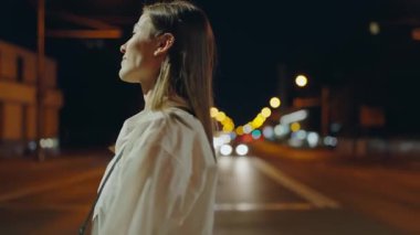 Gece açık havada sakin bir genç kadının portresi, yumuşak odaklı şehir ışıkları güzel bir zemin sağlıyor. Şehirde Huzurlu Bir Gece Gezintisi Yapan Genç Kadın