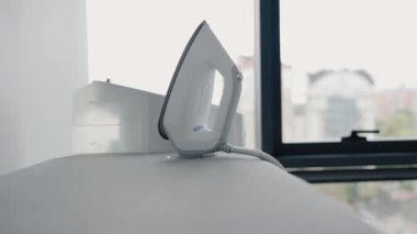 Modern bir buhar ütüsü, minimalist bir evin penceresinin yakınındaki bir ütü masasında bulunur. Çağdaş bir ev ortamında ev işi yapmanın özünü yansıtıyor..