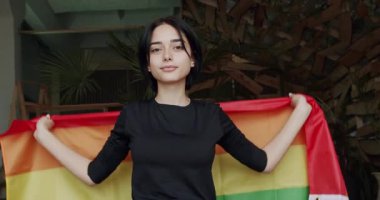 Lgbt kadınları gururlu gökkuşağı bayrağıyla kameraya bakıyorlar. Sarıl ve tut. Mutlu bayan ve gülümse. cinsel çeşitlilik, LGBTQI, Onur Etkinliği, Yaşam Tarzı ve İlişkiler. LGBT kavramı