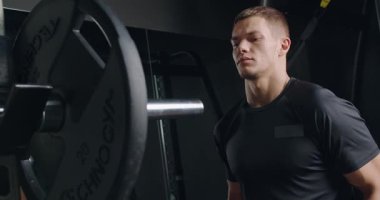 Kararlı genç bir erkek atlet yoğun ağırlık kaldırıyor, gücünü gösteriyor ve iyi donanımlı modern bir spor salonuna odaklanıyor. Modern Spor Salonunda Ağır Ağırlıkları Kaldıran Odaklanmış Genç Adam