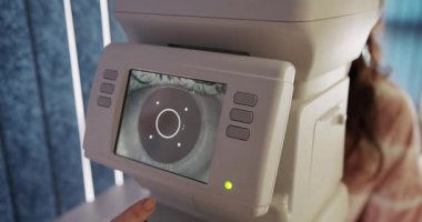 Bir göz kliniğinde gelişmiş optik ekipman kullanan bir kadın hastaya yakından bakmak, göz bakımındaki teknolojik gelişmeleri vurgulamak. Göz Kliniğinde Modern Optik Ekipman Kullanan Kadın