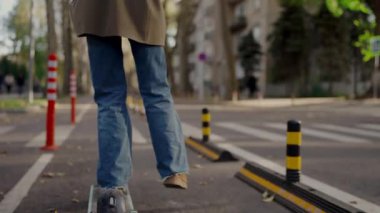Şehirdeki yaya geçidinde düşmüş bir scooter 'ın yanından geçen kot pantolonlu bir adamın yer aldığı şehir manzarası hareketlilik, güvenlik ve kentsel ulaşım temaları öneriyor..