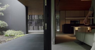 Şık bir adam, gösterişli, çağdaş bir eve girer. Minimalist tasarım, sakin bir bahçe ve sofistike iç mekanlar barındırır. Minimalist Mimariyle Modern Bir Eve Giren Adam