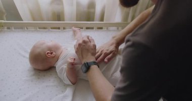 Genç adam baba, bebek odasındaki masajda tatlı bebeğin nazik karnına masaj yapıyor. Baba ve çocuk arasındaki bağı kutluyoruz. Ebeveyn bakımı kavramı. Baba oynuyor ve bebeğe masaj yapıyor..