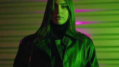 Uzun kahverengi saçlı genç kadın model renkli arka planda poz veriyor. Gece vakti renkli bir arkaplanda kameraya bakan genç bir kadın. Baştan çıkarıcı kadın parlak neon renkli ışıklarla aydınlatılıyor..