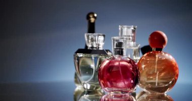 Yansıtıcı bir yüzeyde, zarif bir şekilde aydınlatılmış çeşitli parfüm şişeleri koleksiyonu. Şişelerin çeşitli şekilleri ve renkleri lüks ve güzel kokulu bir atmosfer yaratıyor..